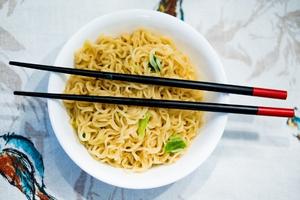 Photo of a bowl of vegetarian Asian noodles with chopsticks laid across it.