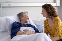 photo of a woman in a hospital bed with a younger woman visiting and the two of them smiling