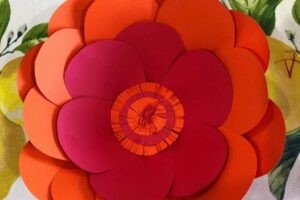 photo of a large paper flower made from orange and red paper on top of a table cloth with lemons.