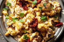 photo of a plate full of grilled cauliflower and chickpeas with tahini, spices and fresh herbs