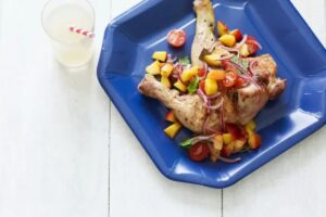 photo of grilled chicken legs topped with peach salsa on a blue paper plate next to a glass of lemonade with a stripped paper straw
