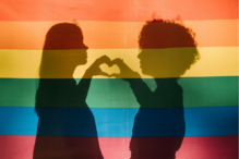 Image of two children's silhouettes holding their hands in a heart shaped formation with the pride flag as the backgrounds