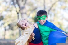 Photo of a girl and boy wearing superhero capes and masks