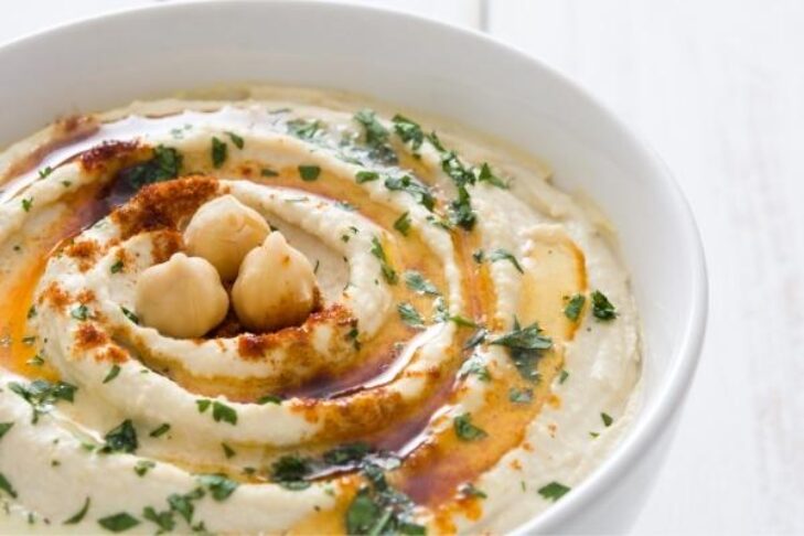 Stock image of hummus in a bowl with parsley, olive oil, chickpeas, and paprika on top as garnish