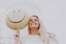 Stock image of a girl smiling and holding up a smiley face balloon