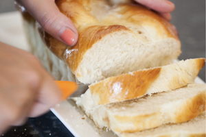 Photo of a woman slicing fresh challah bread