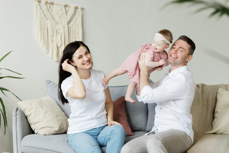 Stock image of a mother and father sitting on a couch holding a baby