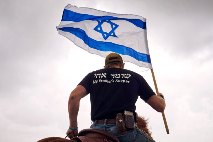 Stock image of a man holding the Israeli flag and his back to the camera - his shirt is in Hebrew