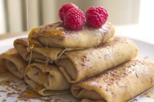 photo of a stack of blintzes on a plate topped with a few raspberries and drizzled with honey