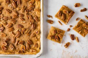 photo of pecan toffee shortbread bars in a ban with three square on the side and a handful of scattered pecans