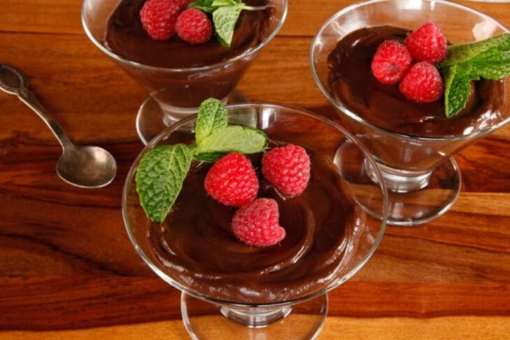 Photo of three glasses filled with chocolate pudding with raspberries and mint on top