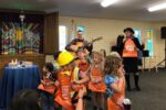photo of kids wearing construction costumes dancing for Shabbat with a cantor playing guitar and a rabbi