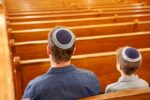 Stock image of a father and sun wearing kippahs in a synagogue