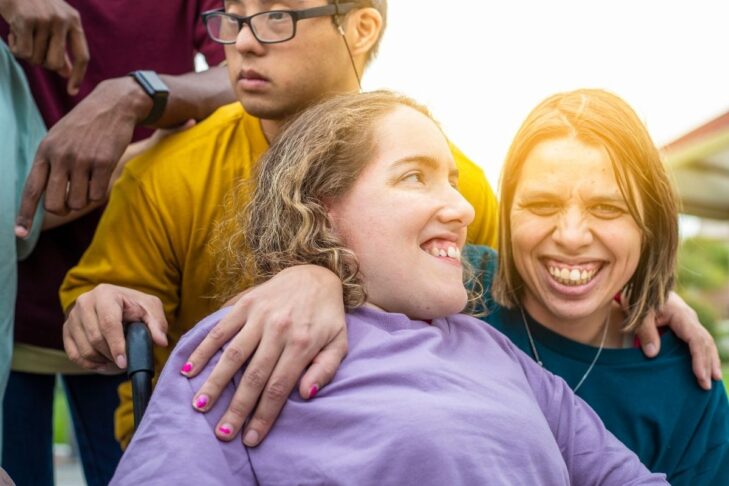 photo of a group of friends with one person in a wheelchair and another with their hand around their shoulder in a warm embrace