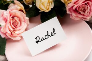 photo of a pink plate on a table with a few pink and yellow roses and a place card with the name Rachel written on the card