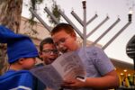 Photo of, from left, brothers Meir, 7, Yossi, 9, and Tzemach Levertov sing songs during a celebration for the first night of Hanukkah at the Biltmore Fashion Park on Sunday, Nov. 28, 2021, in Phoenix. The event was hosted by Chabad Lubavitch of Arizona.