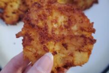 photo of an apple cheddar latke being held up with more in the background on a plate