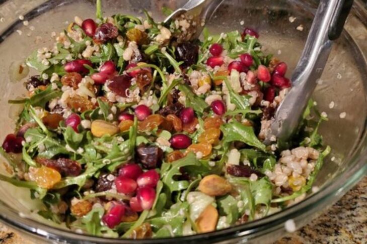 photo of a bowl of seven species salad including raisins, dates, pomegranate seeds, quinoa, barley, arugula, cucumber, and pistachios