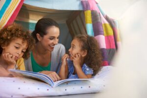 photo of two kids and an adult reading together in a blanket fort