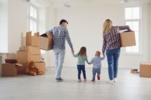 photo of an empty house with moving boxes and a family holding hands