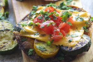 photo of a grilled vegetable tostada topped with cheese, tomatoes and herbs