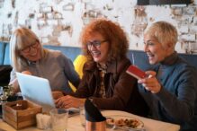 photo of three ladies at lunch smiling and engaging with a computer presentation