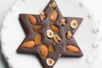 photo of a chocolate in the shape of a Jewish star with pieces of nuts and candied fruit on a white plate