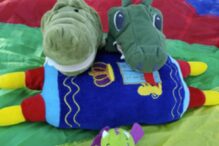 photo of a crocodile and dinosaur stuff on top of a stuffed torah laying on a parachute