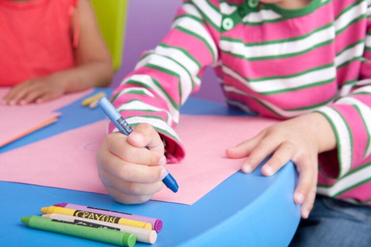 photo of a child holding a blue crayon and coloring on a piece of paper