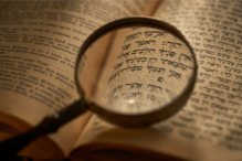 Image of a magnifying glass zooming in on a book of Torah