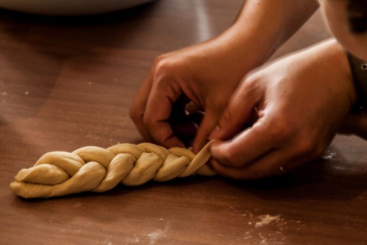 photo of a person braiding a challah on a wood surface