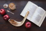 Image of apples, a glass of wine, and a shofar sitting on a siddur