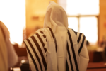 Image of a person wearing a tallit praying in a synagogue.
