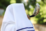 Image of a man blowing a shofar with a tallit over his head