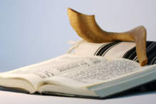 Image of a shofar sitting on an open prayer book with a tallit behind it