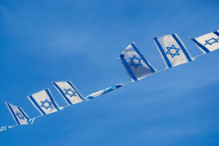 Israeli flags blowing in the wind with a clear blue sky as the background