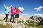 image of three women at the summit of a hike holding hands and raising their arms with their backs facing the camera